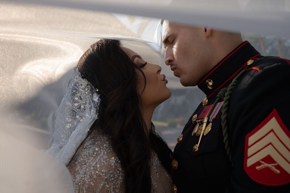 Intimate moment between newlyweds with veil detail and military dress uniform.