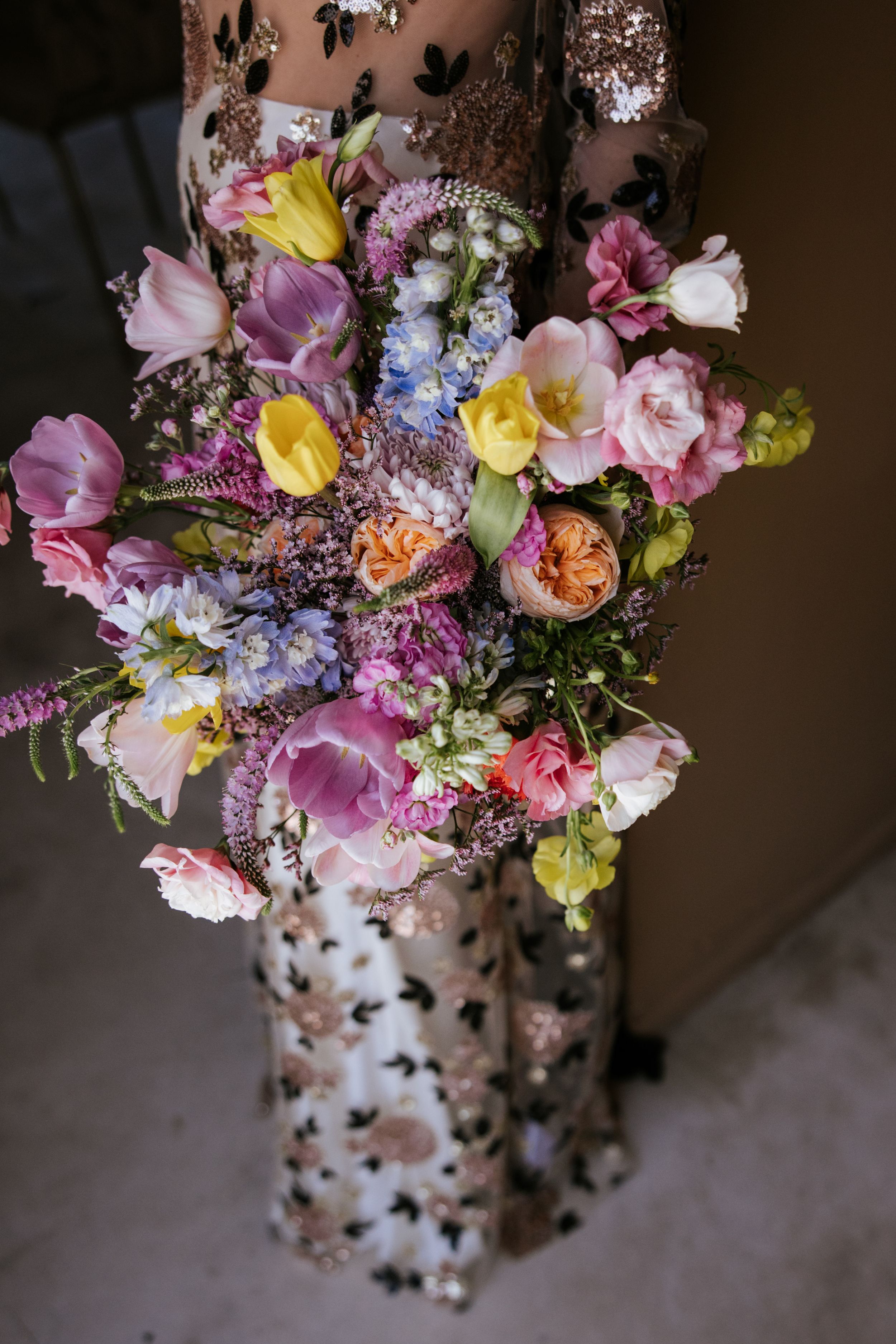 pectacular bridal bouquet filled with delicate, colorful flowers, with the bride's original and authentic wedding dress softly visible in th