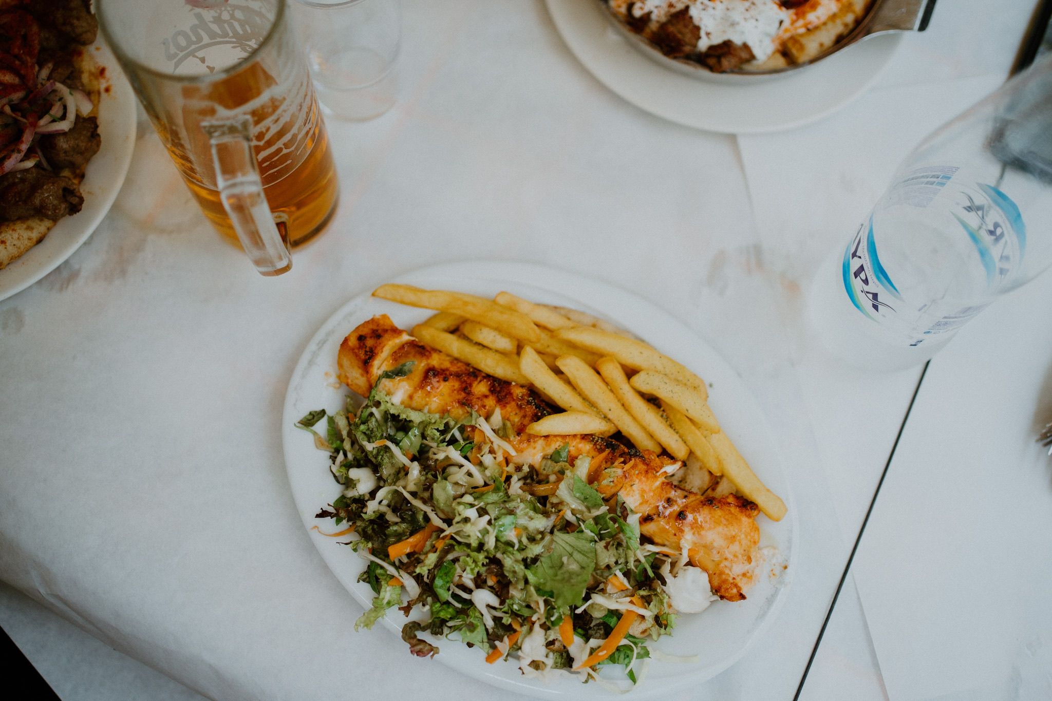A plate of crispy french fries served alongside a fresh green salad and grilled protein on a white tablecloth.