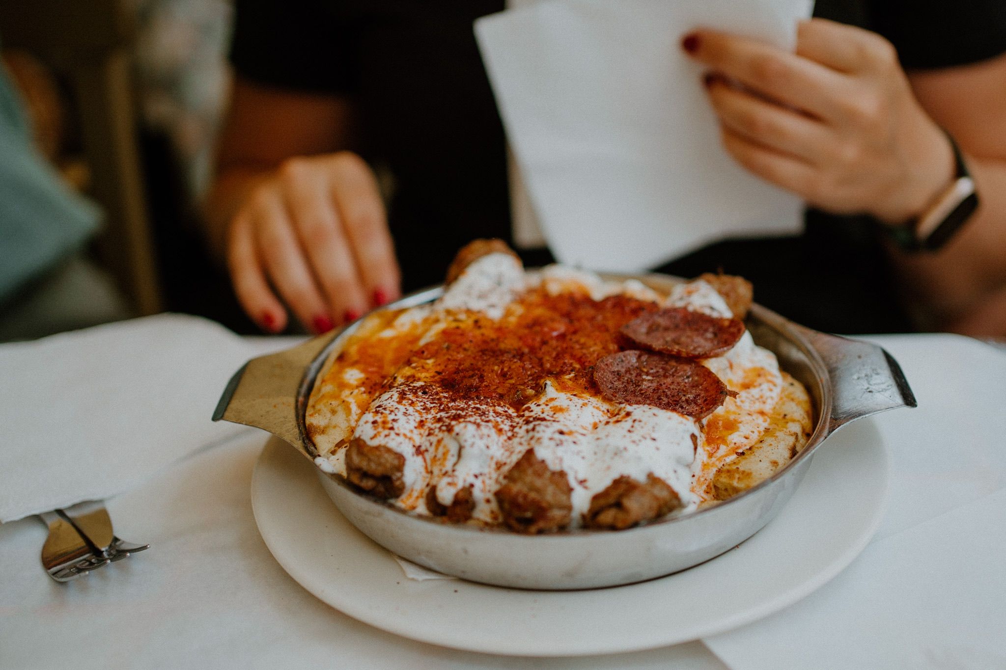 A plate of hot skillet kebab smothered in greek yoghurt and topped with diced pepperoni and sauce.