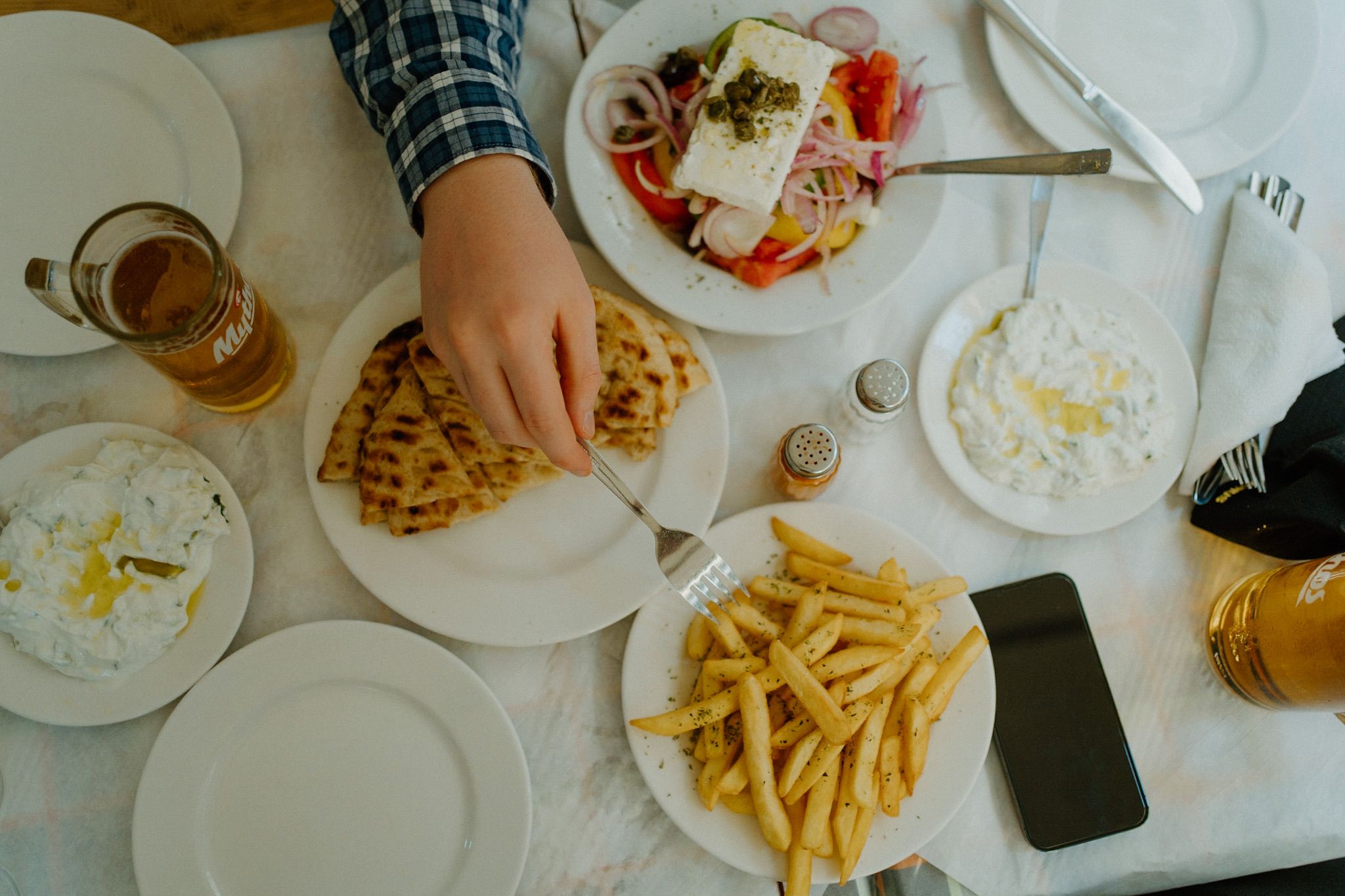 Overhead view of a casual restaurant meal with french fries, salad, and beverages on white plates on a wooden table.