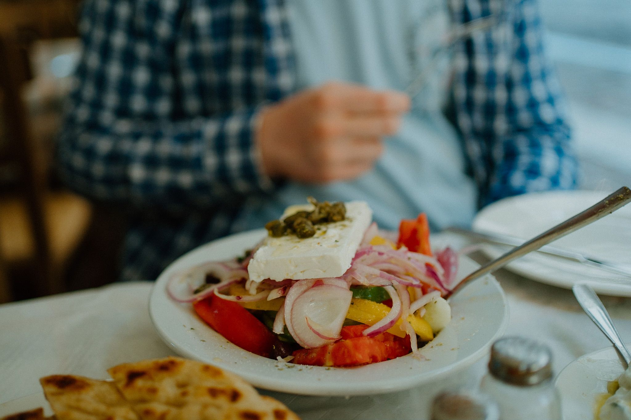 A fresh Greek salad with feta cheese, tomatoes, and red onions served in a white bowl next to pita bread.