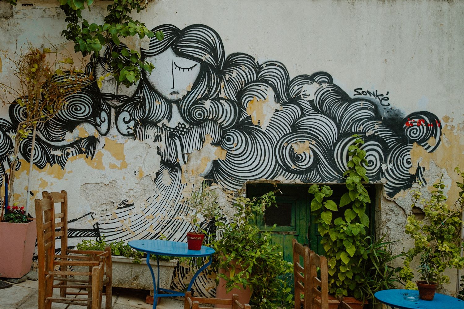 Artistic black and white street art mural of an abstract figure with swirling cloud-like patterns adorns an outdoor wall.