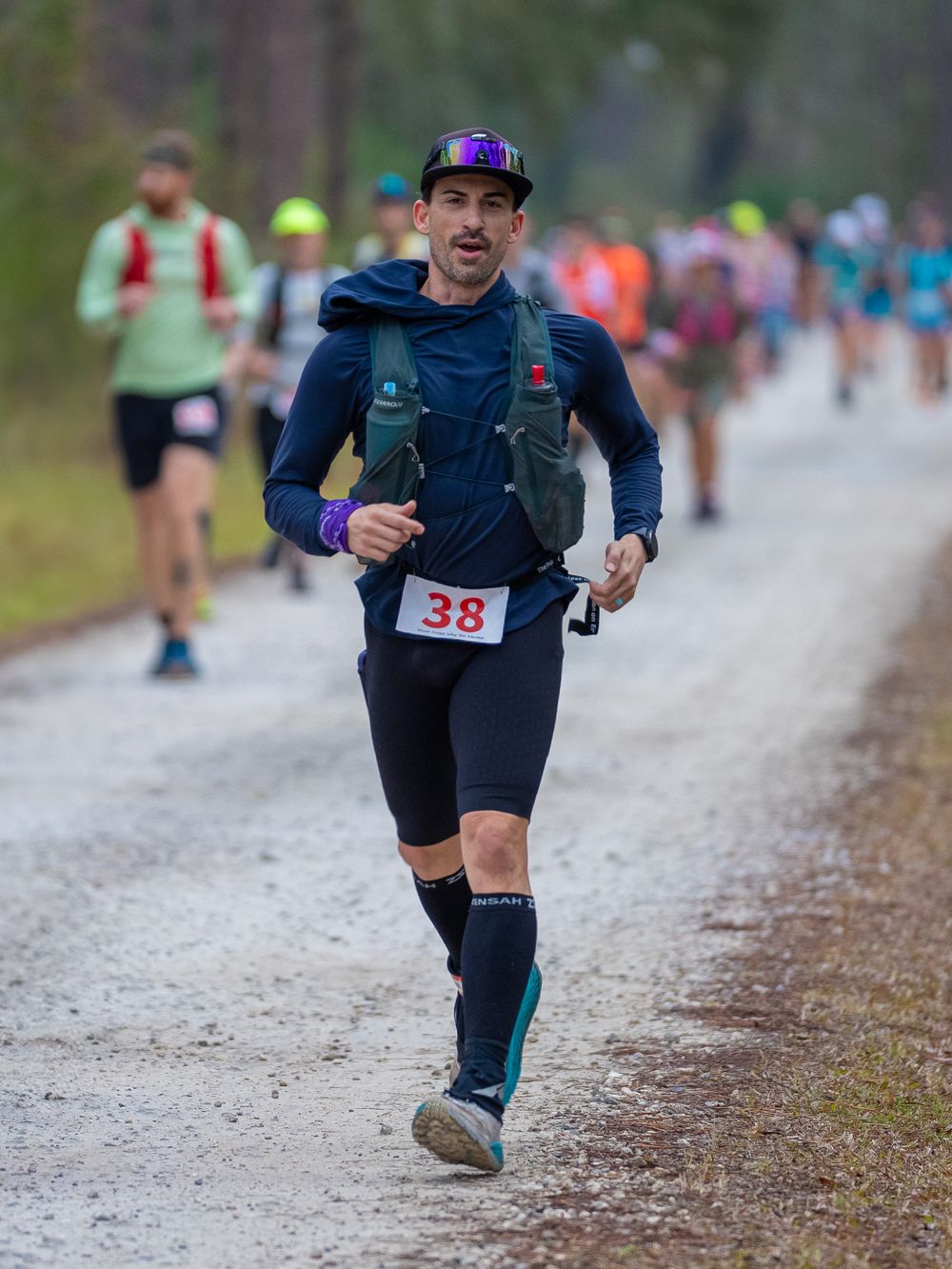 Trail runner in navy athletic gear with race number 38 competes on a wet gravel path.