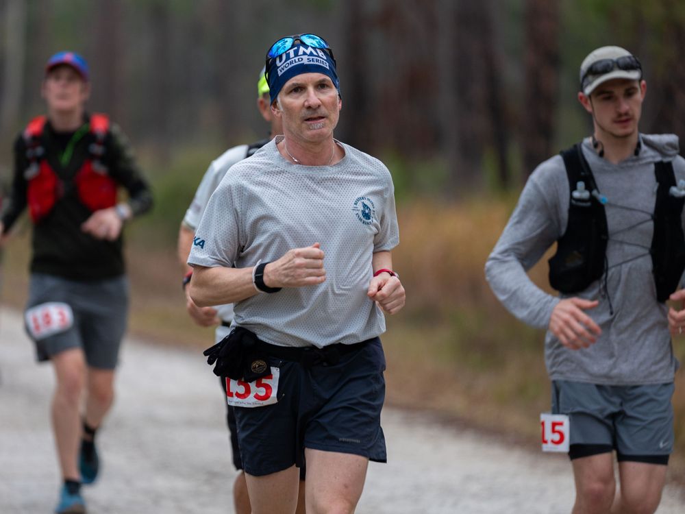 Runners compete on a pine tree-lined trail during an endurance race event.