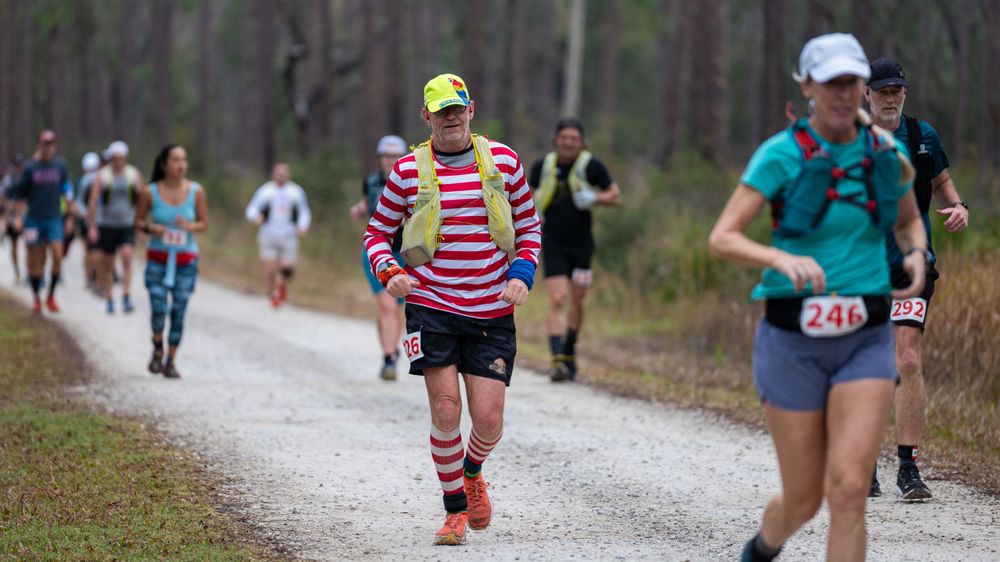 Trail runners in colorful gear navigate a white gravel path through pine forest.