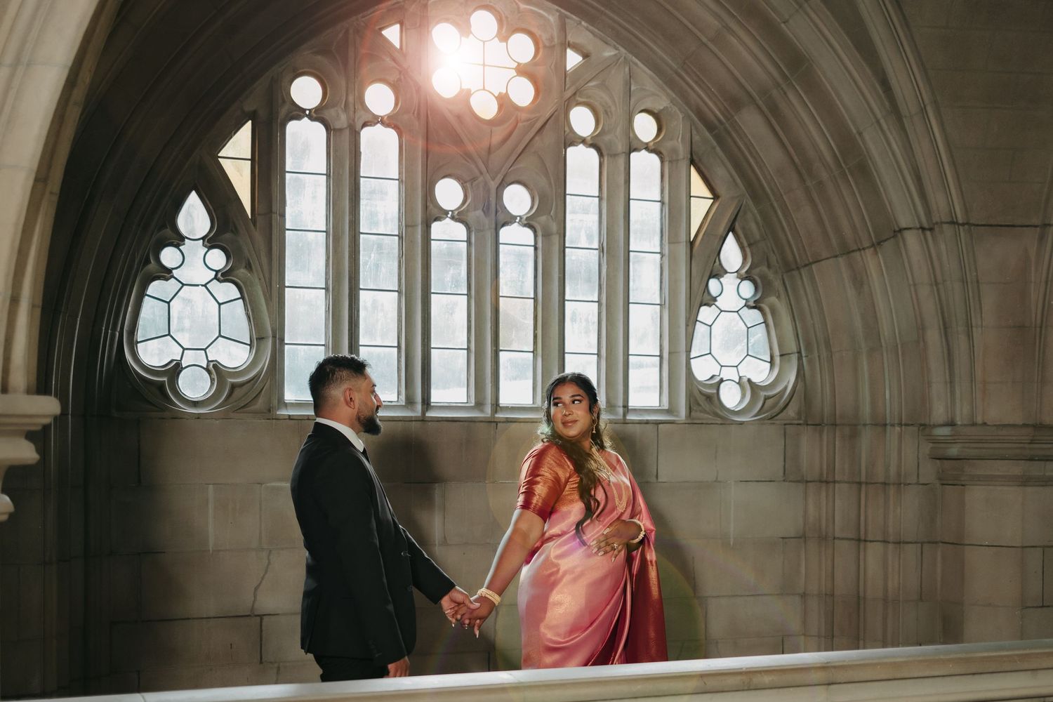 A couple stands in a gothic cathedral hall with beautiful stained glass windows and arched architecture.