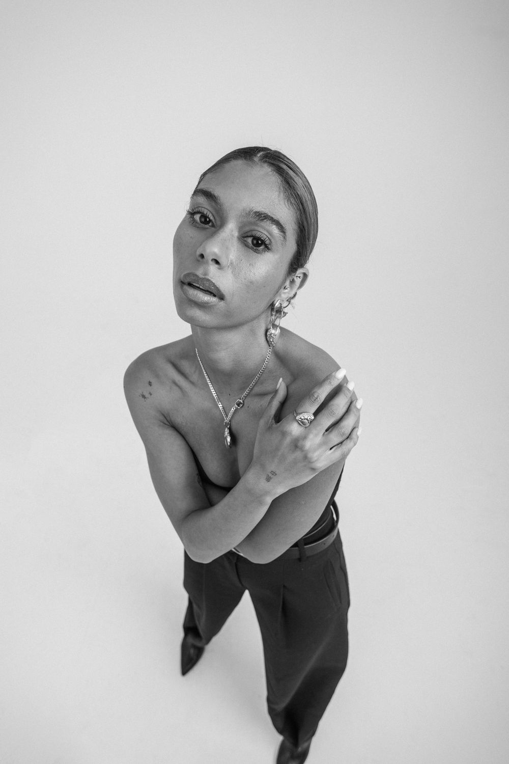Black and white artistic portrait from above shows a person in minimalist setting wearing black outfit and jewelry.