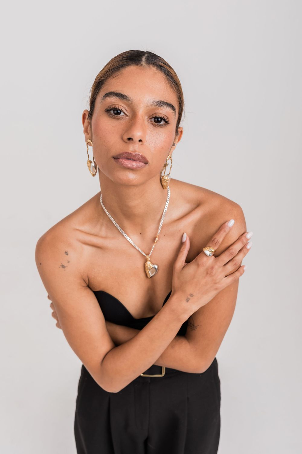 A model poses in a black strapless dress with silver jewelry against a light gray background.