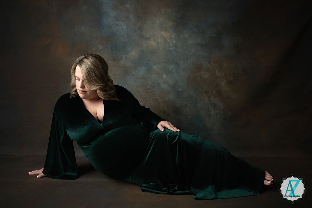 Artistic portrait of a figure in an elegant emerald velvet dress reclining against a dark moody backdrop.