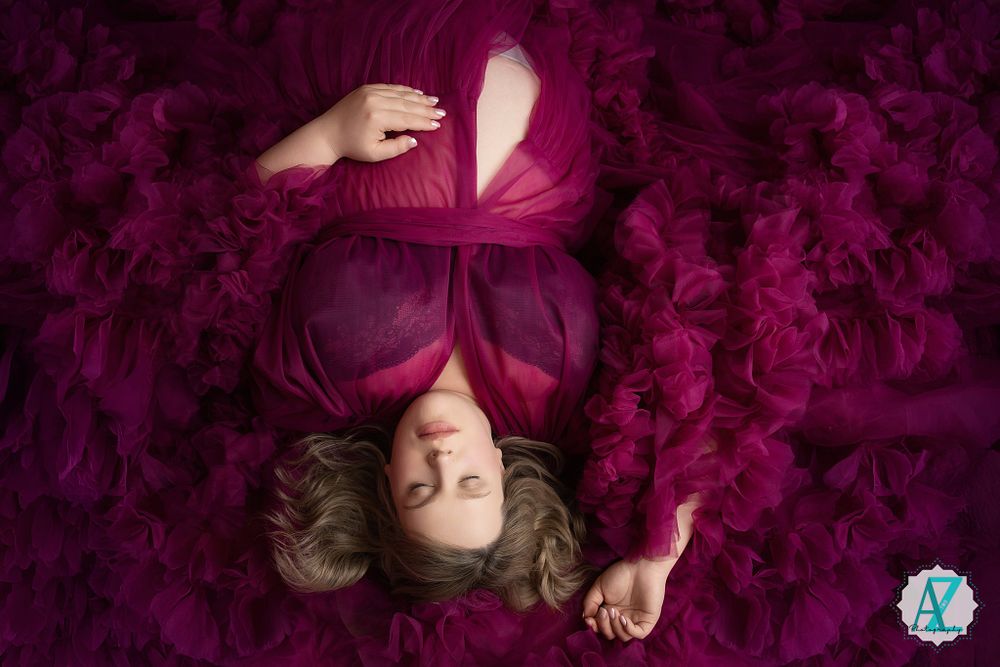 Artistic portrait with subject laying on purple textured fabric wearing a red dress and surrounded by vibrant magenta colors.