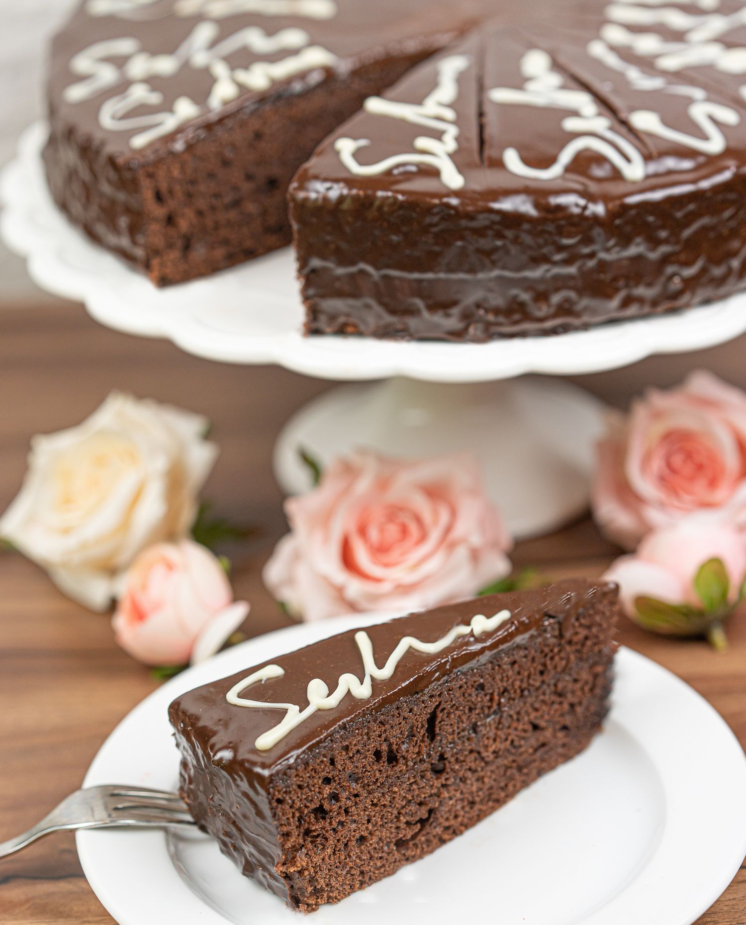 Foodfotografie - Slice of chocolate Sacher torte with decorative icing served with pink roses.