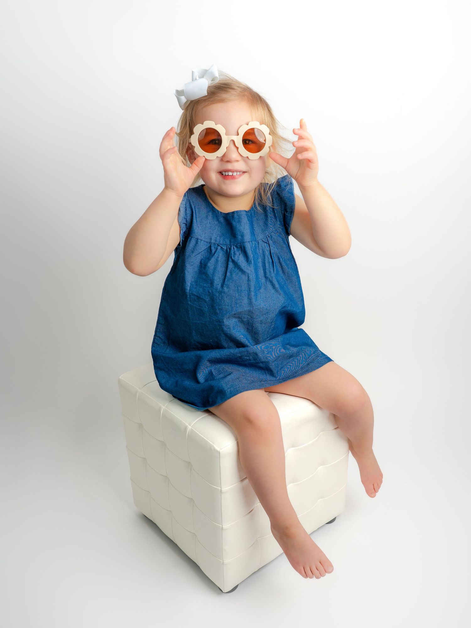 Photo of a little girl with a denim dress sitting on a white ottoman taken by Dandridge TN family portrait photographer