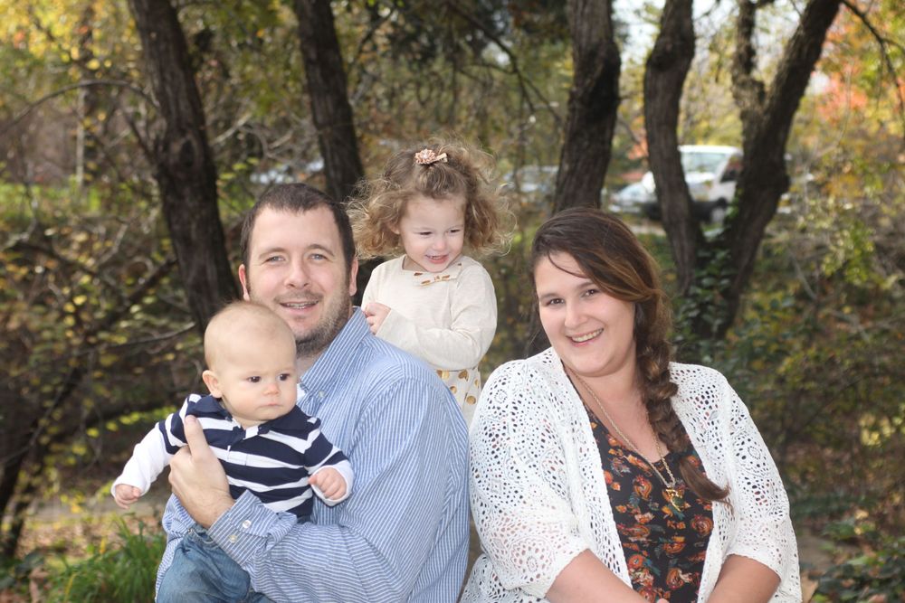 A happy family poses outdoors in autumn with trees and foliage in the background. Family portrait.