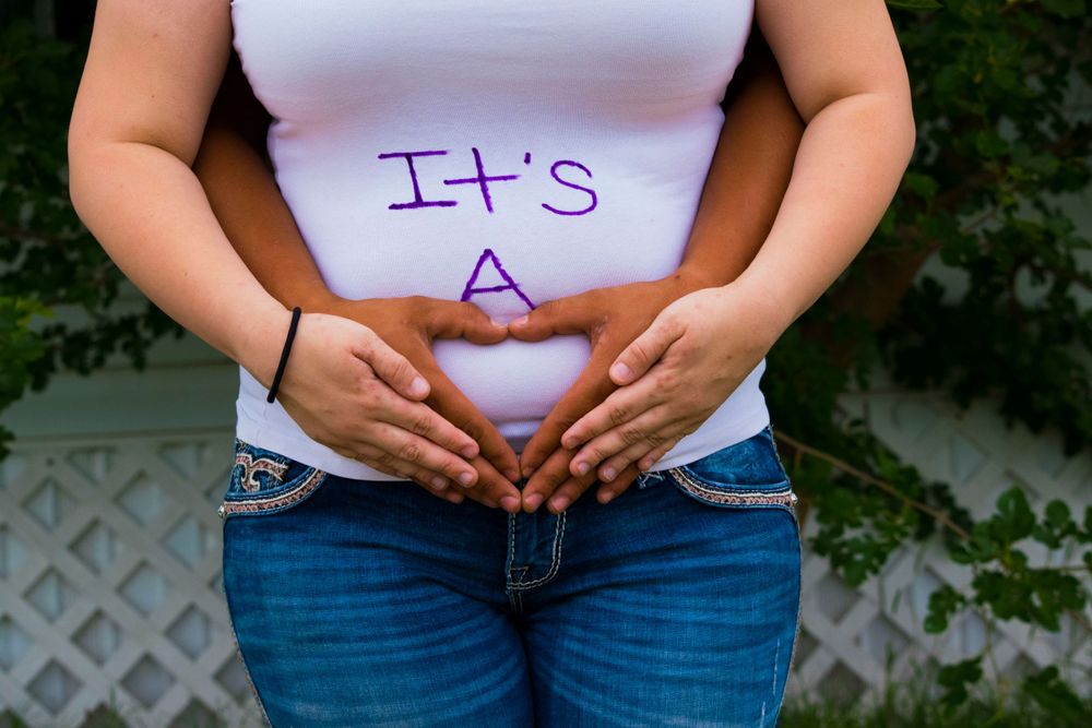 A happy pregnant woman with hands raised, displaying "It's a girl" for a joyful baby girl announcement.
