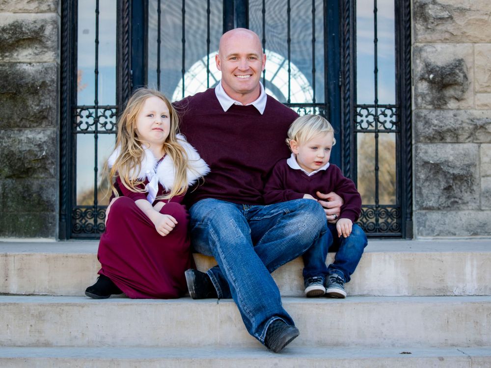 A father and his two children, a silly girl and a detached boy, sit together on the steps, sharing a lighthearted moment.
