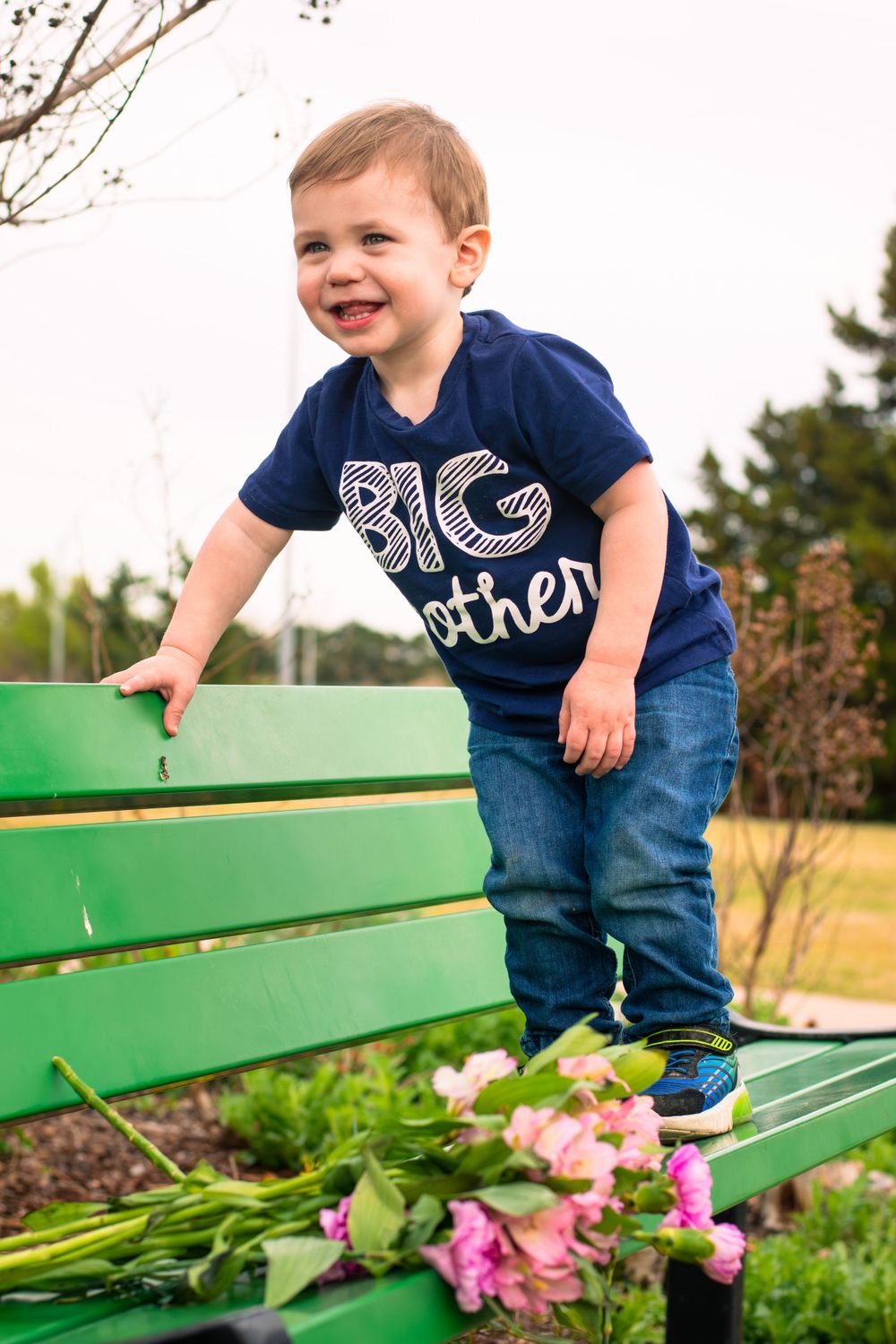 A young boy on a bench with vibrant flowers, symbolizing the joyful announcement of a new baby girl in the family.
