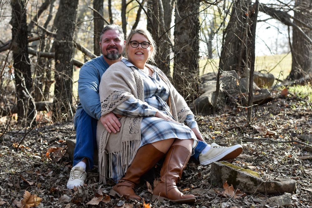 A man and woman sit together on a rock in a serene forest, surrounded by trees and nature's tranquility.