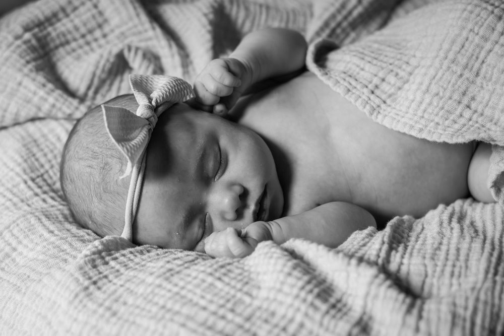 Infant wearing a bow headband, sleeping peacefully wrapped in a textured blanket.