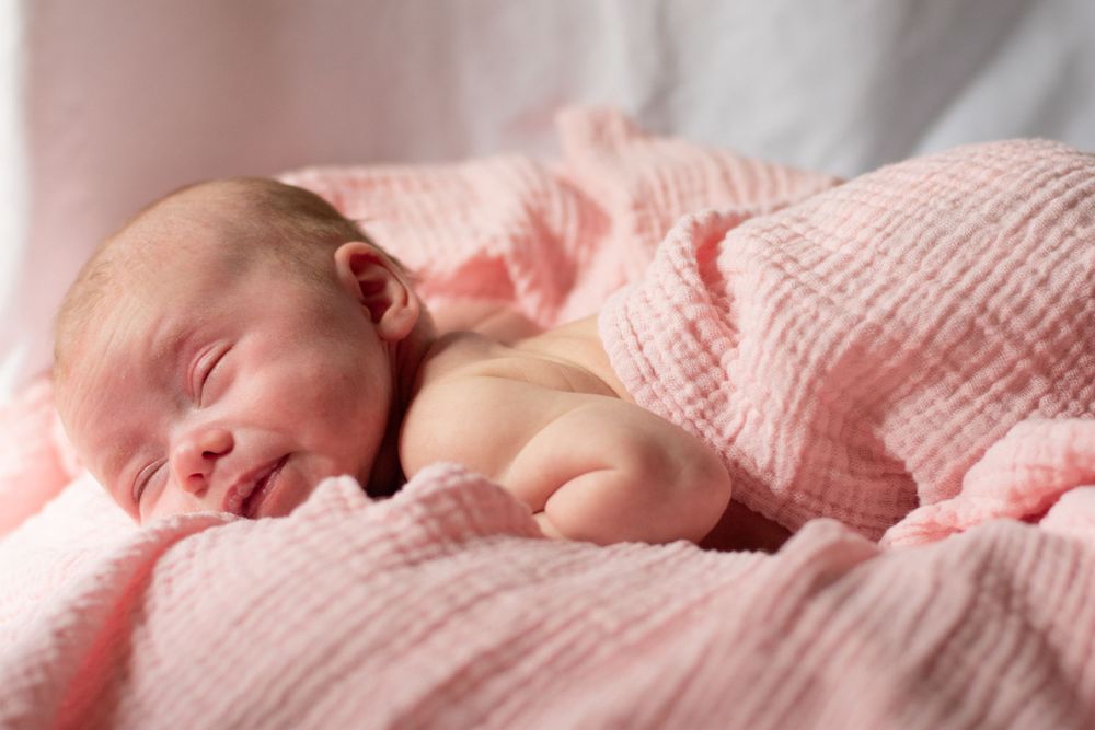 Newborn baby girl wrapped in a soft pink textured blanket, sleeping peacefully.