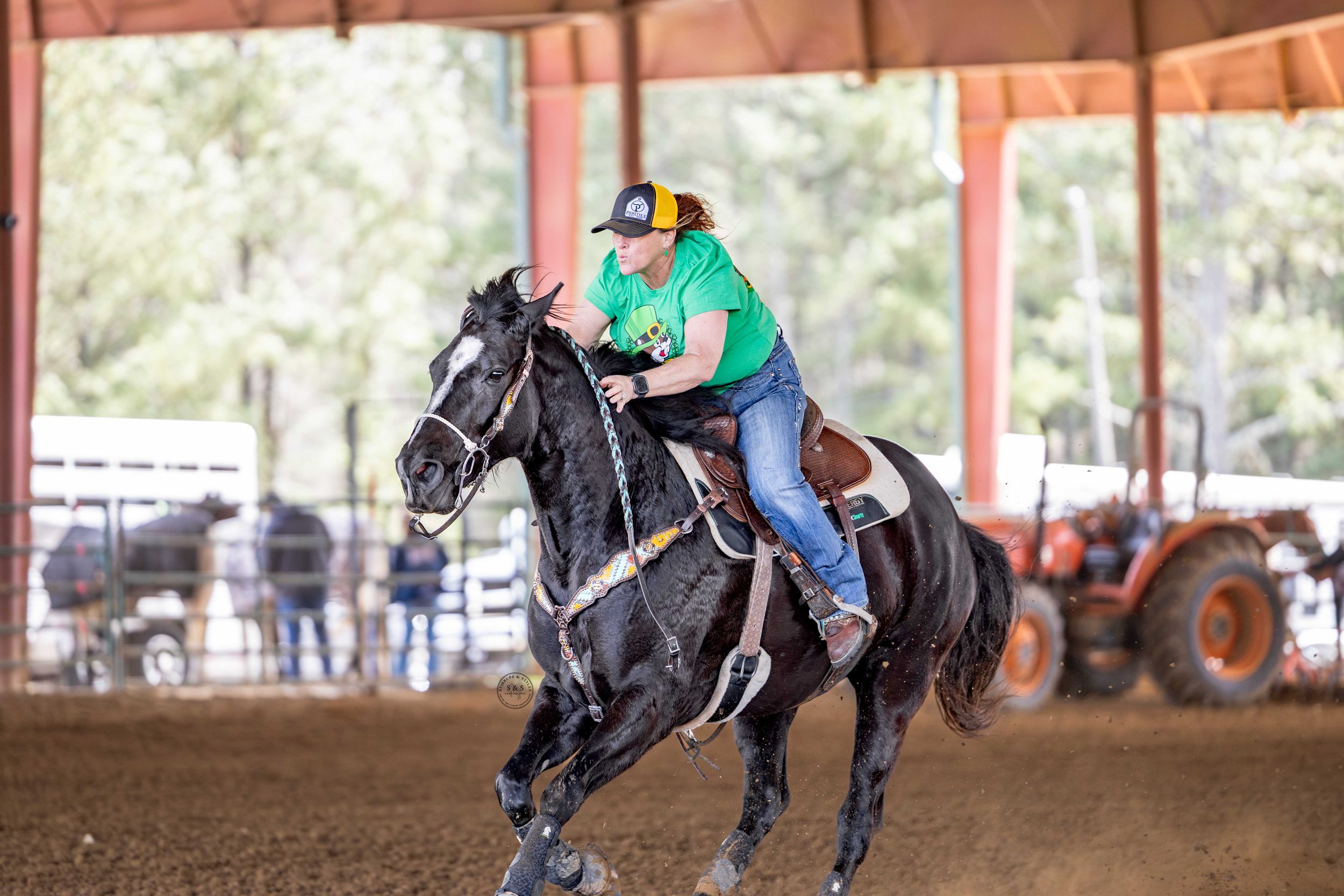 A rider in turquoise shirt guides a black horse through a covered arena during equestrian training.