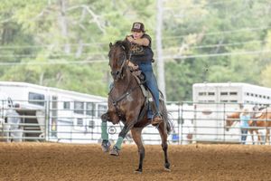 A rider on horseback kicks up dust while barrel racing in an outdoor rodeo arena.