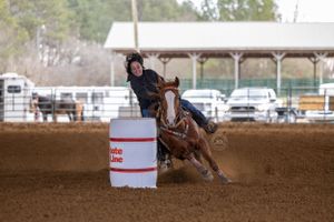 A competitive barrel racer navigating their horse around a barrel in a dusty arena.