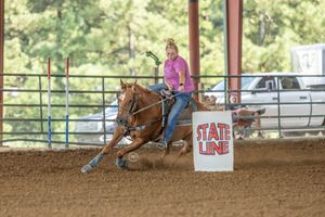 A pair of barrel racers compete on horseback in a dirt arena during a rodeo competition.