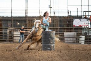 A barrel racing competitor and horse make a tight turn around a barrel during a rodeo competition.