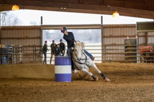 A horse and rider performing a barrel racing run in an indoor arena setting.