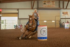 A horse and rider compete in barrel racing, making a tight turn around a barrel in an indoor arena.