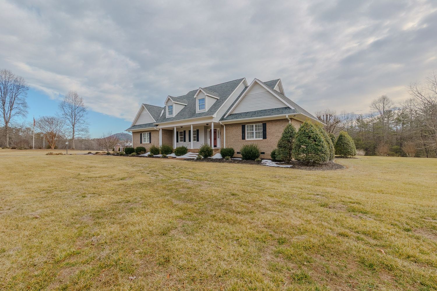 Charming Cape Cod style home with covered porch and American flag surrounded by mature landscaping.