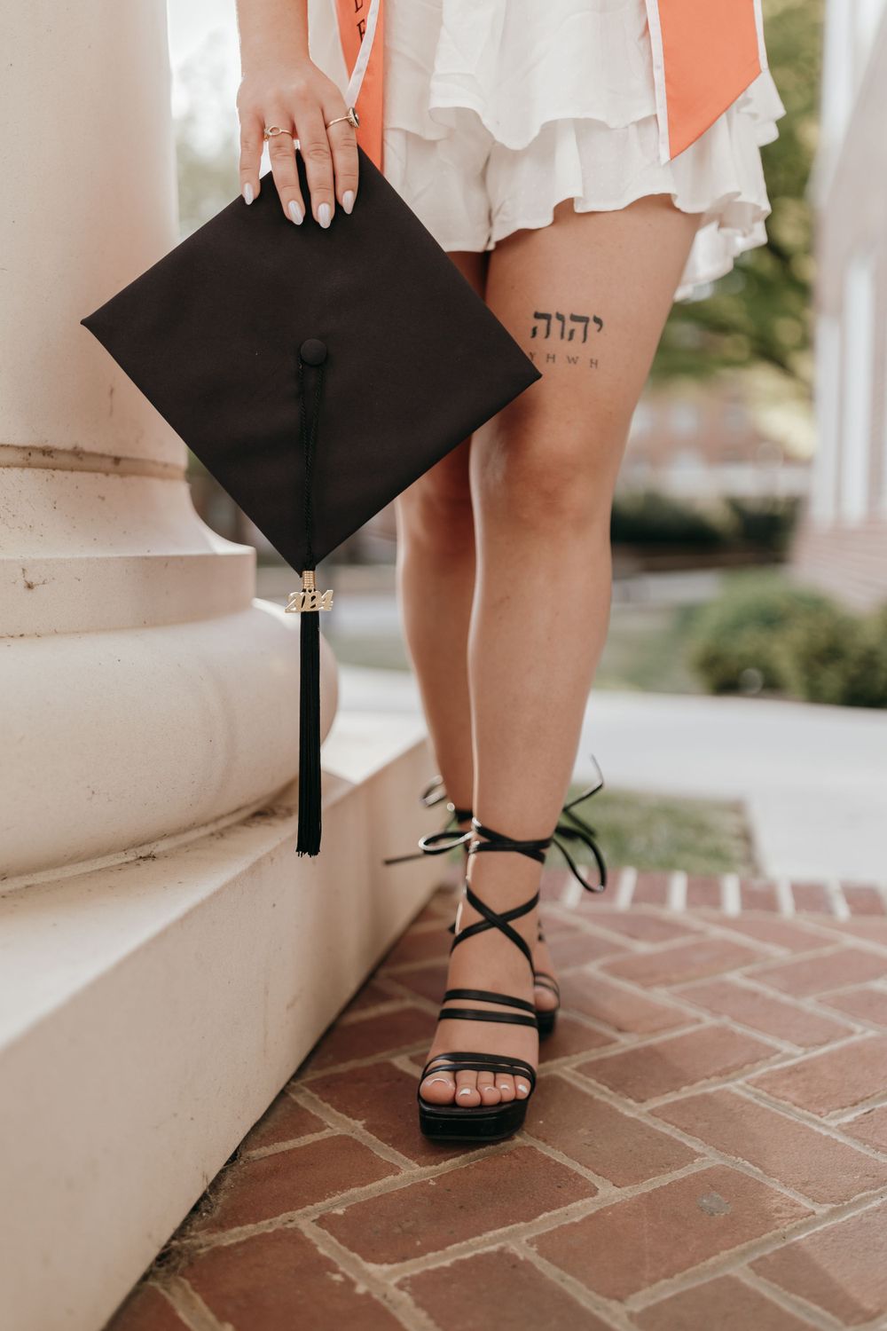 Close-up of graduation cap and strappy sandals with Hebrew tattoo visible on leg. Virginia graduation/senior session.