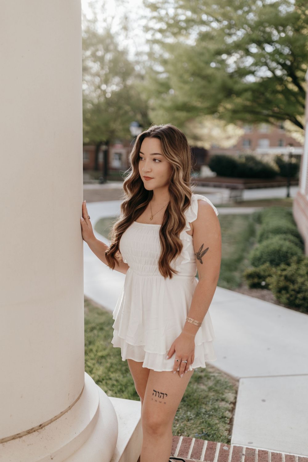 Graduate in white sundress poses against classical column showing Hebrew script tattoo. Virginia graduation/senior session.