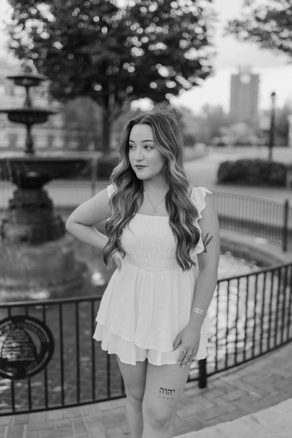 Black and white graduation photo of a person in a white dress standing by a fountain on a university campus. Virginia graduation/senior sess