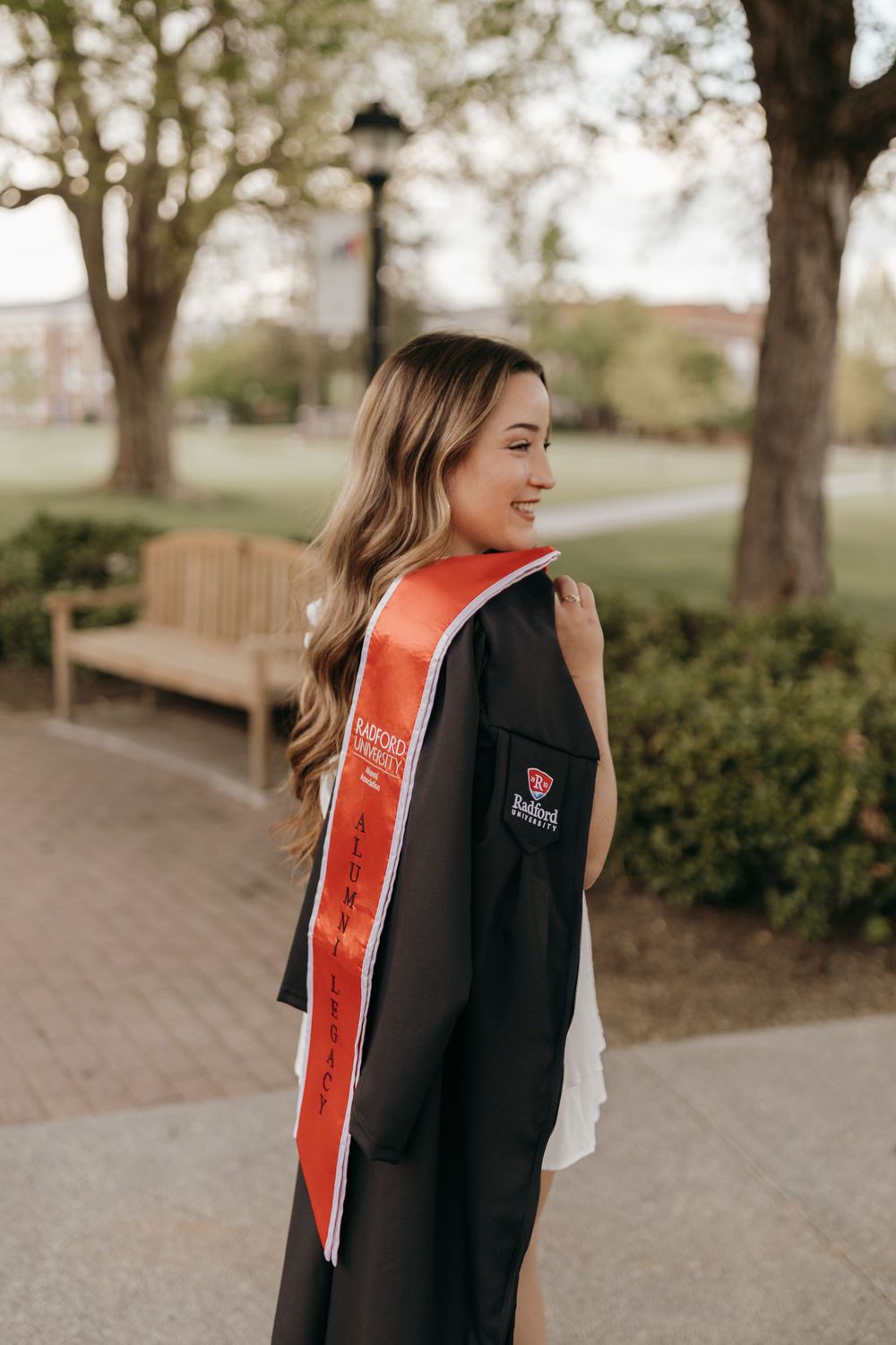 Side view of graduate wearing academic regalia and stole against campus pathway and trees. Virginia graduation/senior session.