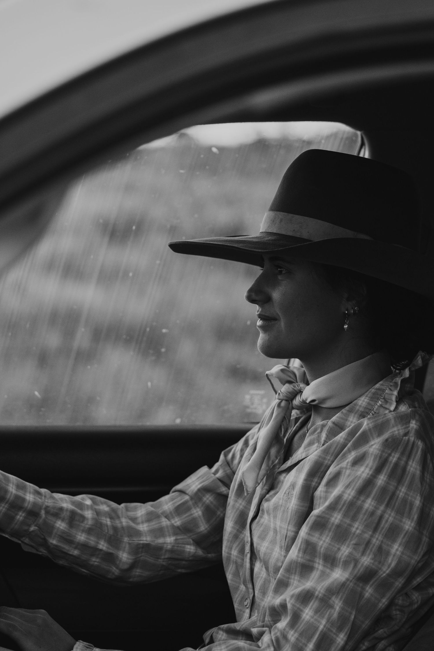 Classic black and white portrait of someone in a cowboy hat driving a car in the rain.