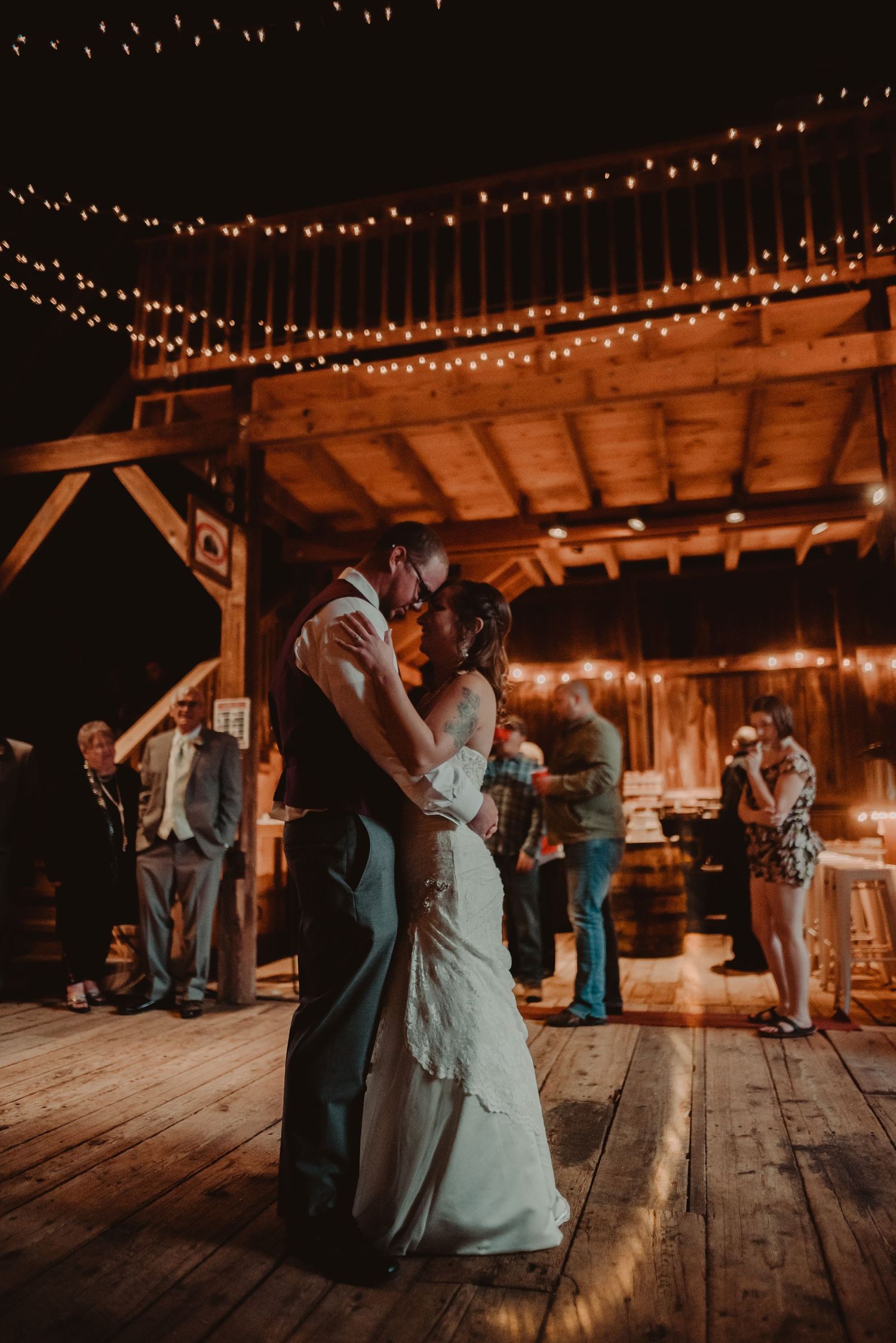 Romantic first dance at rustic barn wedding reception under glowing string lights.