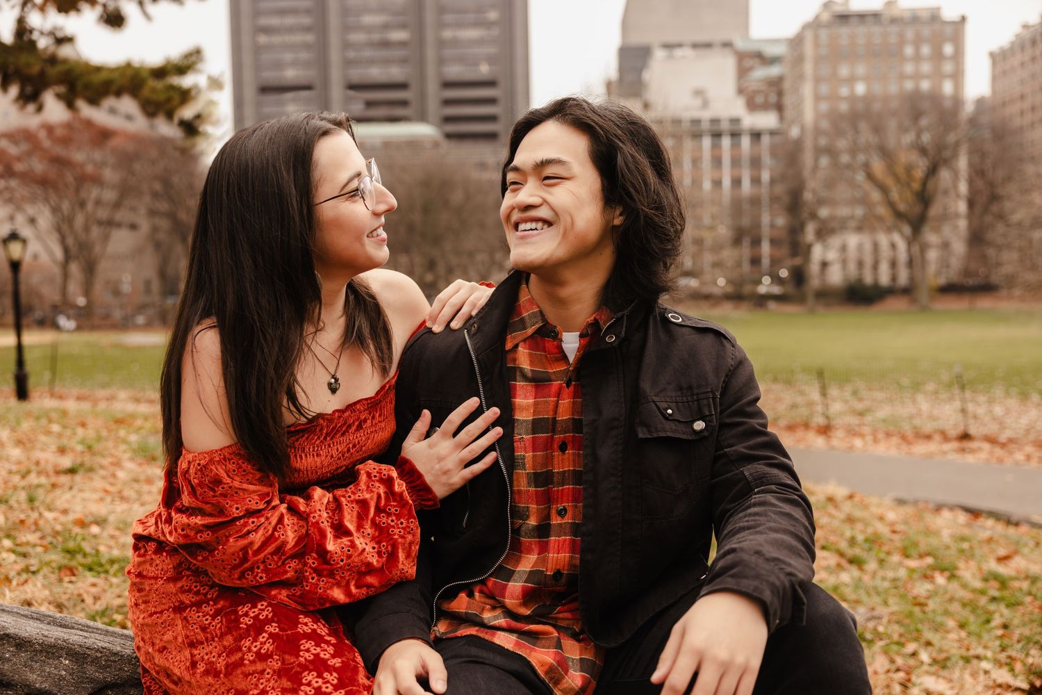 A couple shares a joyful moment while sitting outdoors in autumn.