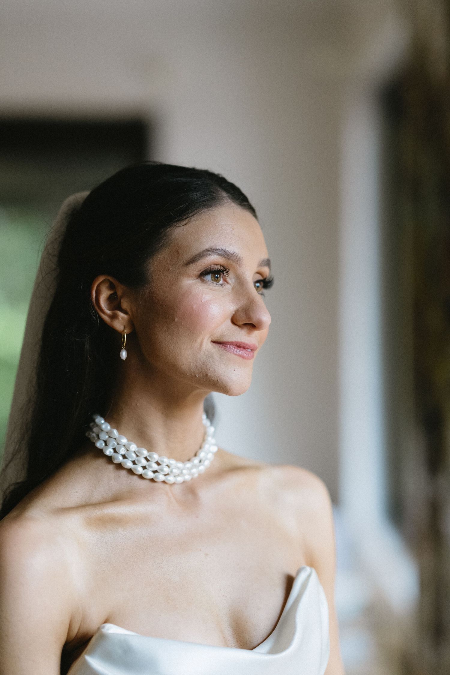 Elegant bride in strapless gown with pearl necklace gazes to side.