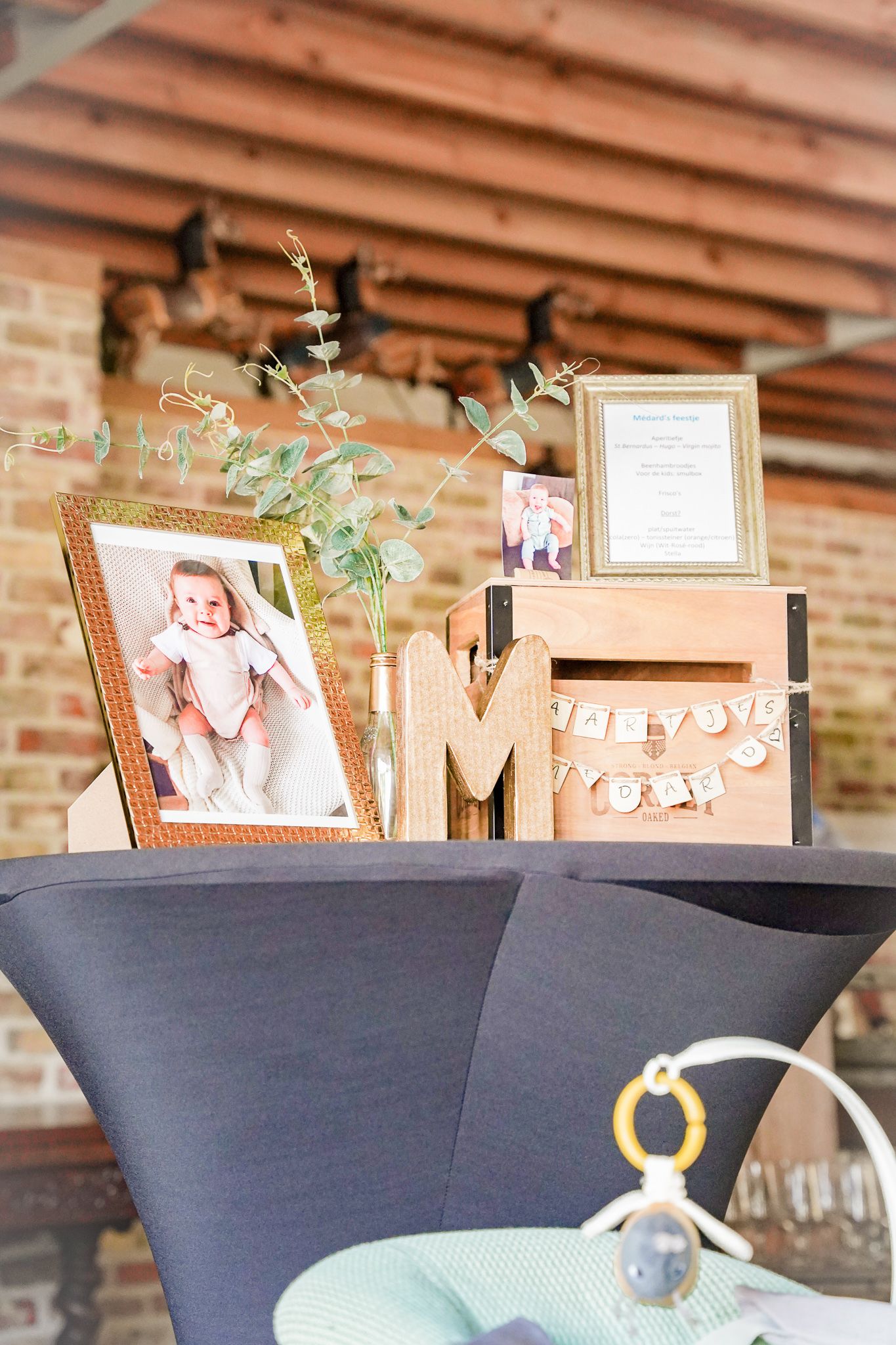 Rustic party decor featuring framed photos, wooden letters and eucalyptus on dark tablecloth.