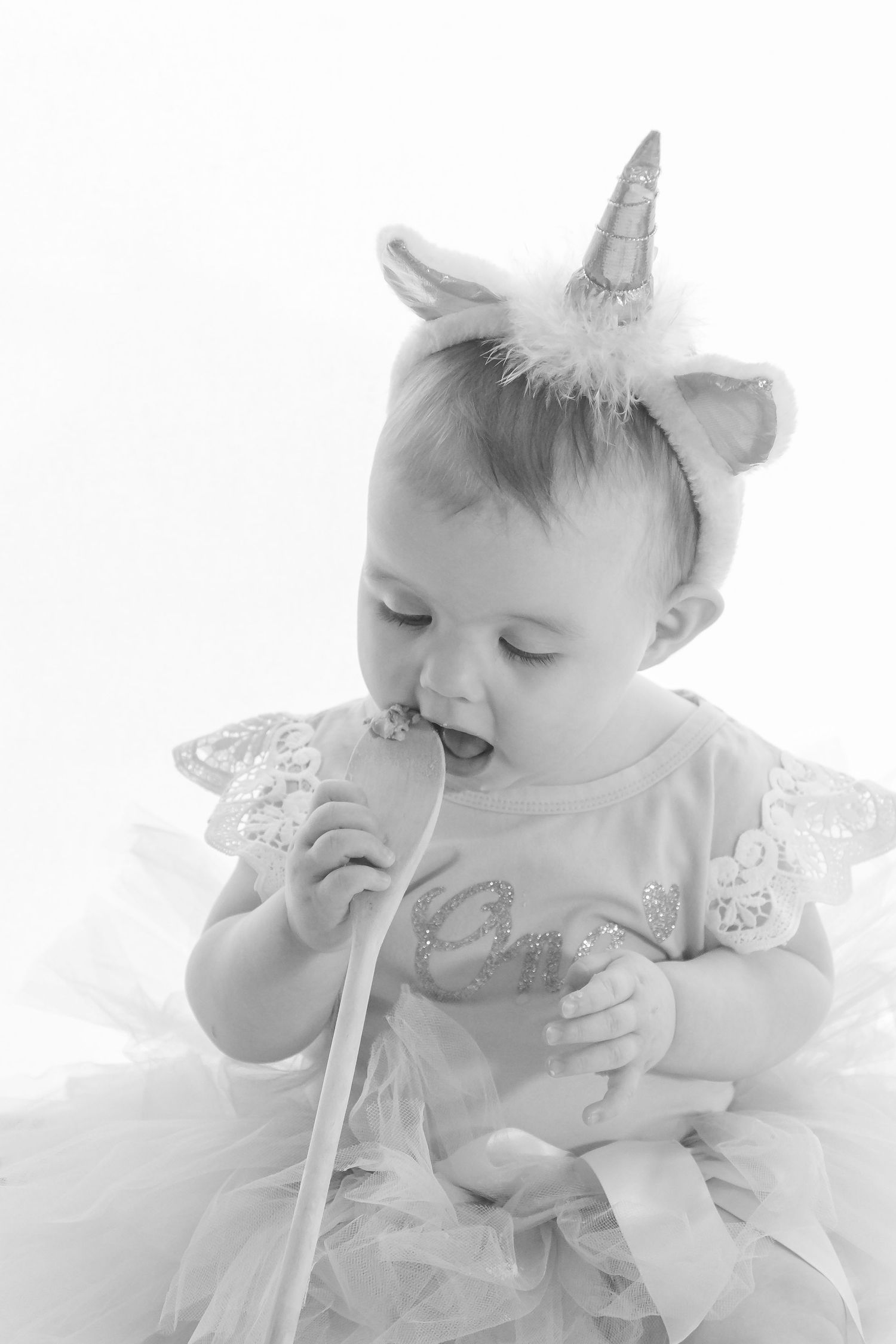 Baby wearing unicorn headband and tulle dress in black and white portrait.