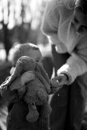 A tender black and white moment between a small child holding a stuffed toy elephant and an adult in winter clothing.
