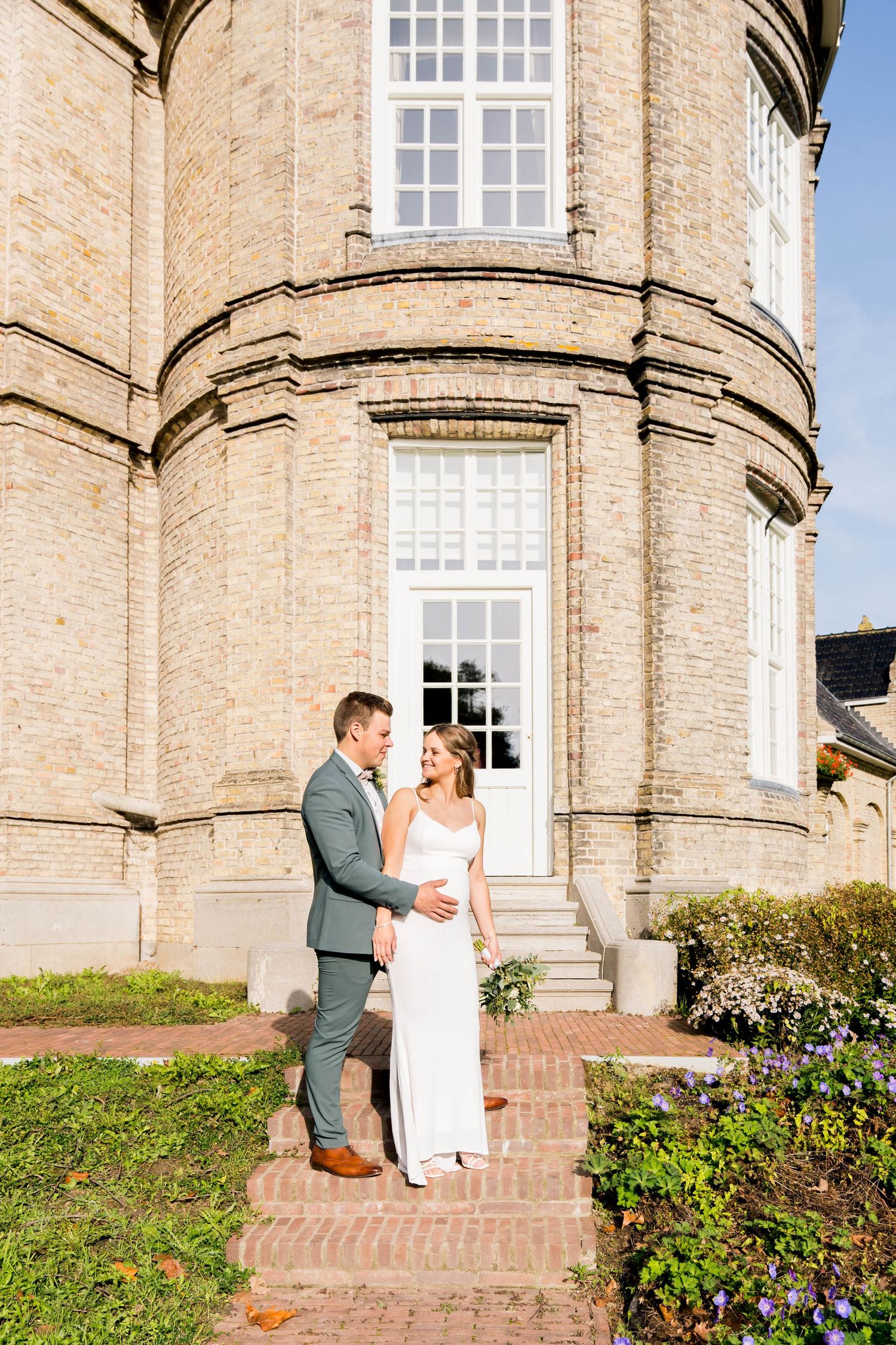 A couple standing in front of an elegant curved brick building with tall windows.