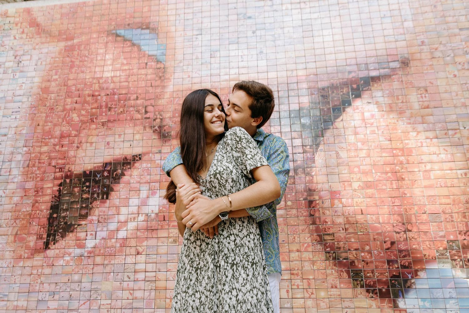 Couple embraces against a pink brick wall in a romantic photoshoot sequence.