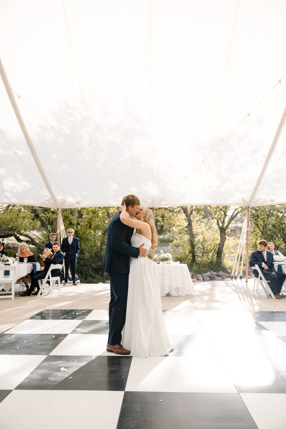 Bride and groom share first dance on checkered floor under elegant tent at outdoor wedding reception.