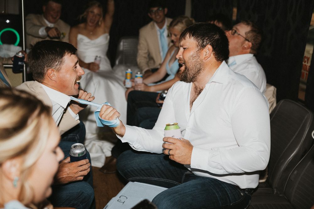 Two men laughing and celebrating at a wedding reception, holding drinks and enjoying the festive atmosphere.