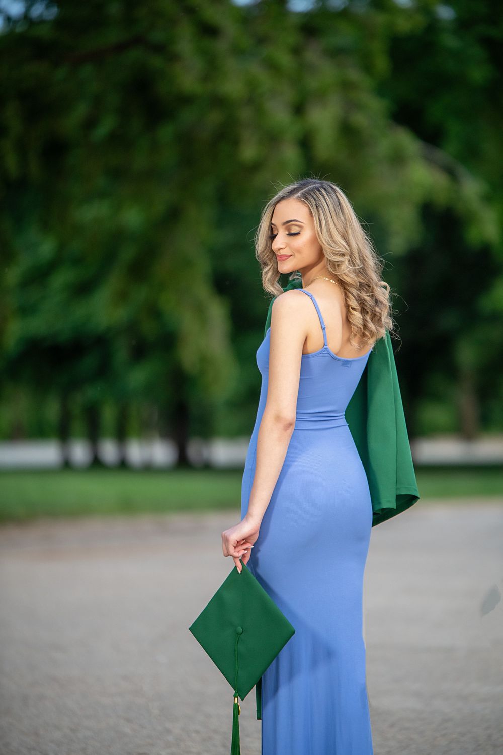 Graduate holding cap while wearing blue dress in park setting.