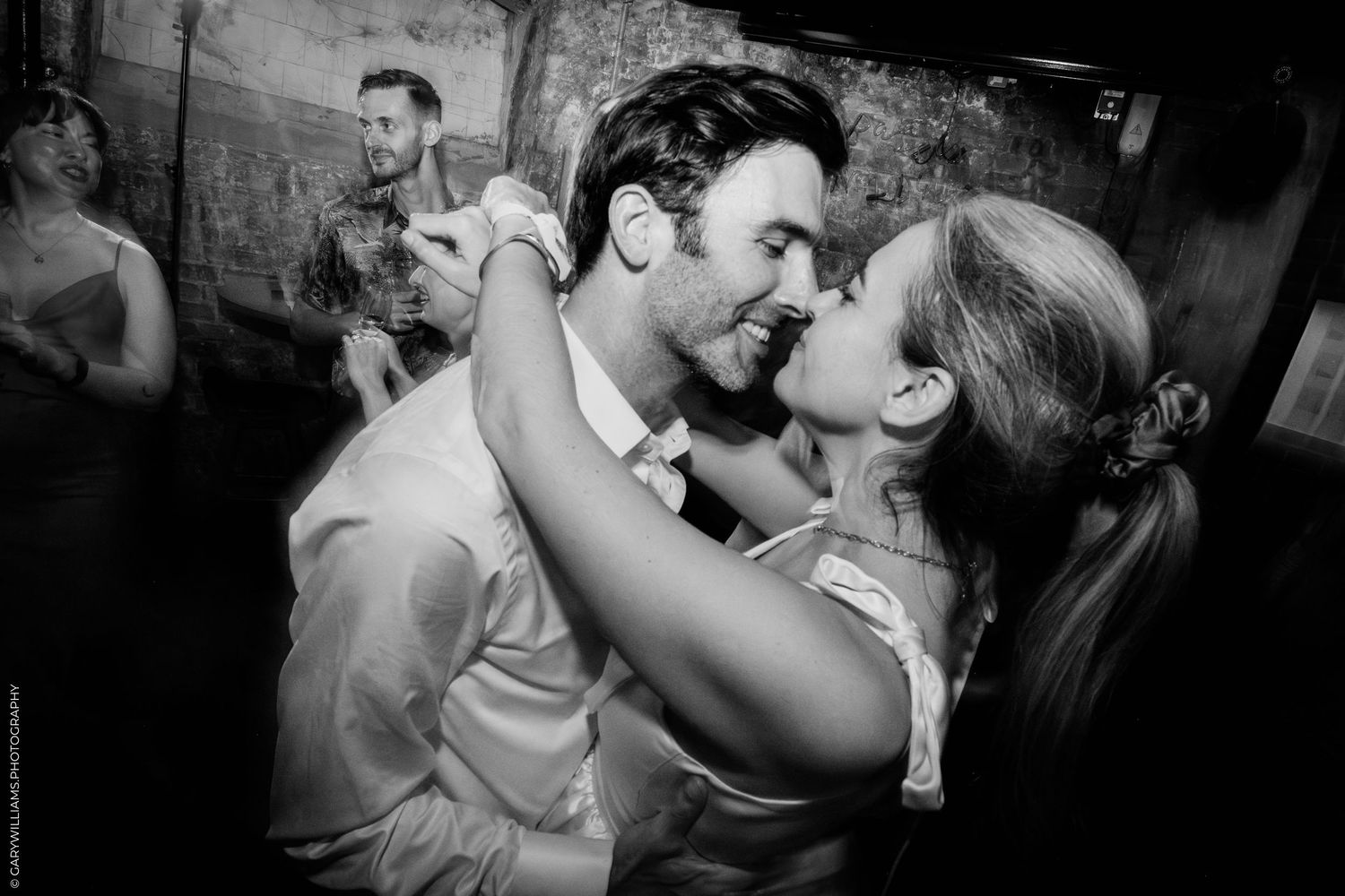 A romantic black and white photograph showing a passionate dance moment between two people at a dimly lit venue.