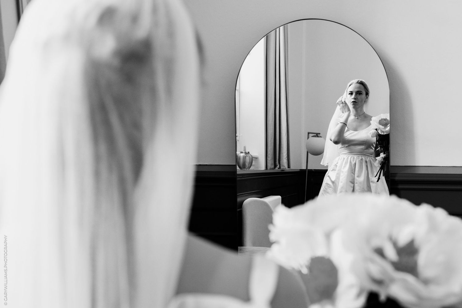 A reflection in a bathroom mirror shows a person in wedding attire making final preparations.
